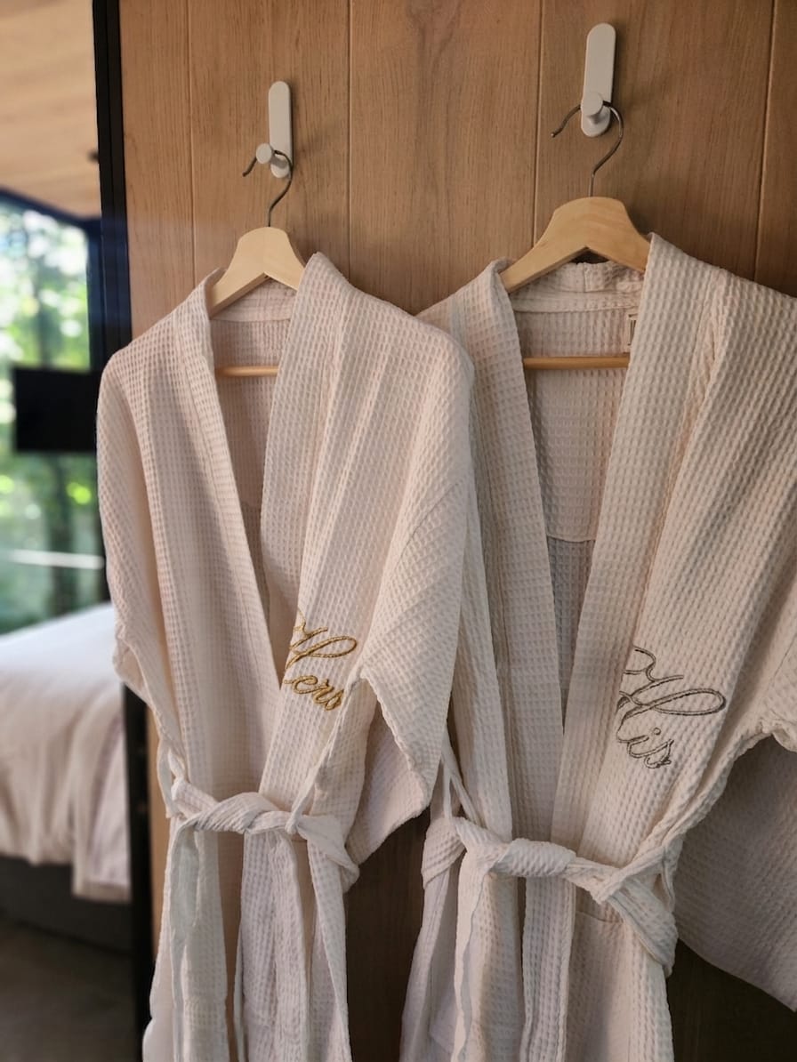 His & Hers waffle robes hanging in the bedroom with gold embroidery